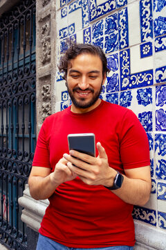 Hispanic young man using smartphone leaning against traditional Talavera tile wall