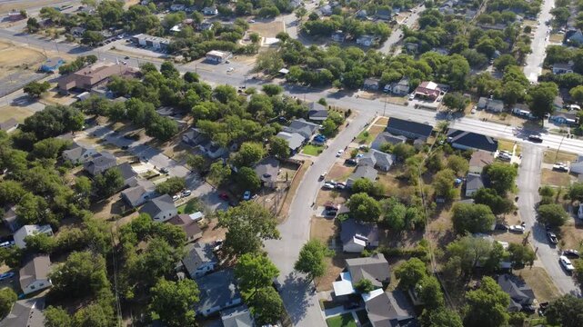 Paved neighborhood streets cross tree-lined subdivisions across DFW suburbs. Clustered single-family houses border wide arterial roadways beneath sunny blue skies, Fort Worth, Texas