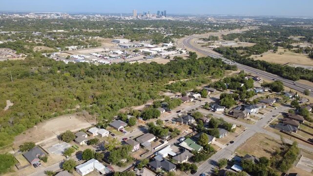 Active home construction frames rising timber structures across Historic Southside. Quiet residential streets border vast natural greenway forests under clear skies, Fort Worth, Texas