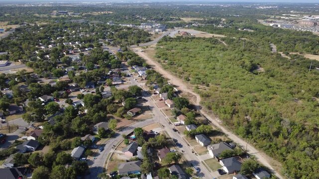 Unpaved boundary road separates suburban residential yards across Historic Southside. Dense natural woodland canopies extend toward distant modern apartment complexes, Fort Worth, Texas