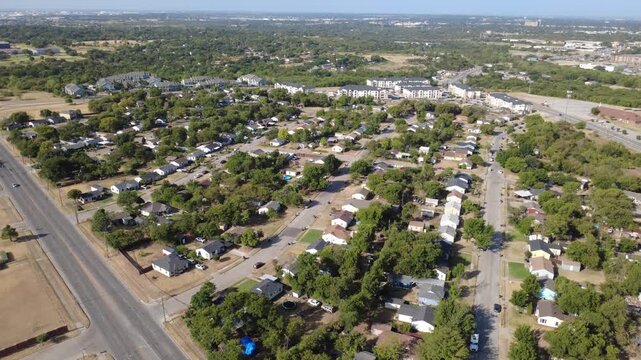 Angled residential avenues cross quiet subdivision blocks across DFW suburbs. Modest single-story homes border modern apartment complexes beneath clear blue skies, Fort Worth, Texas