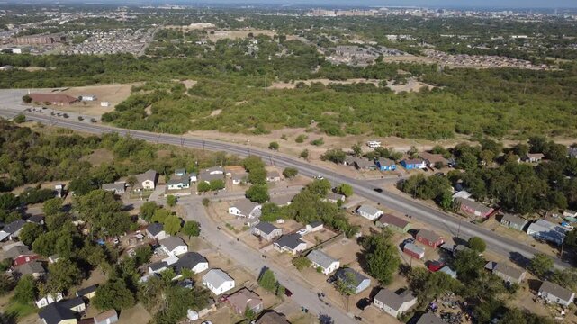 Curving two-lane roadway borders quiet residential enclaves across Tarrant County. Fenced suburban backyards meet expansive natural greenway spaces under bright sun, Fort Worth, Texas