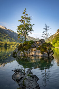 Bewachsene Felseninsel im Hintersee bei Ramsau im Hochformat mit Wasserspiegelung.