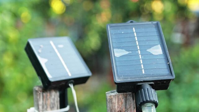 Close-up of small solar panels mounted on wooden stakes in a garden during daytime, showcasing alternative energy and eco-friendly technology. Mini solar panel generating clean energy