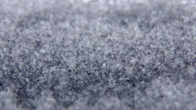 Close-up macro shot of textured snow crystals glistening under bright light, creating a crisp and abstract winter background. frozen ice crystals and snowflakes with a white winter texture background