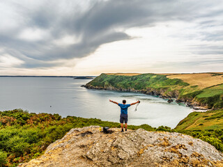 Naklejka premium Men on rocks over Cornwall Cliffs and Farms from a drone, Polruan, Cornwall, England