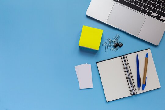 Flat lay of student desk with laptop notebook sticky notes pens on bright blue background computer notebooks