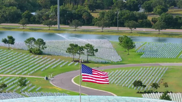 Military burial headstones. Sarasota National Cemetery with rows of white tomb stones and USA flags on green grass. Memorial Day concept.