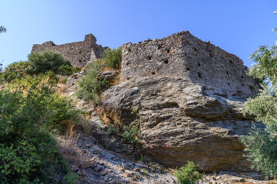 Rubble stone wall of the Castle of Agia Paraskevi rising from bare rock, seen from below through olive branches, Laconia, Greece