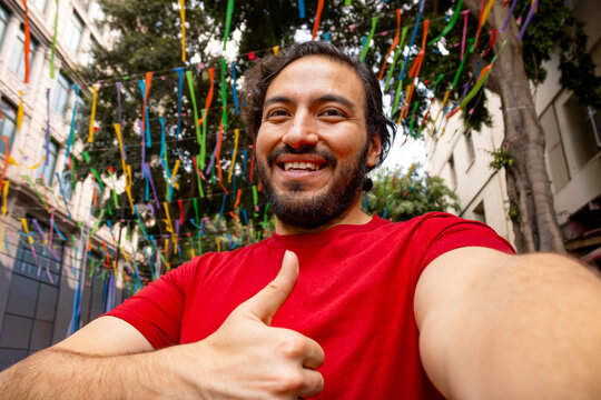 Happy young man taking a selfie with thumbs up on a festive street