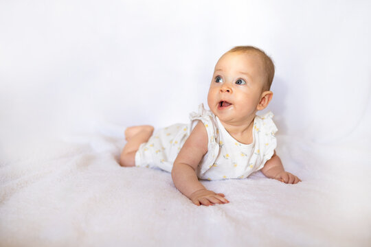 Baby girl in white sunny bedroom. Newborn child relaxing in bed. Nursery for children. Textile and bedding for kids. Family morning at home. New born kid during tummy time.