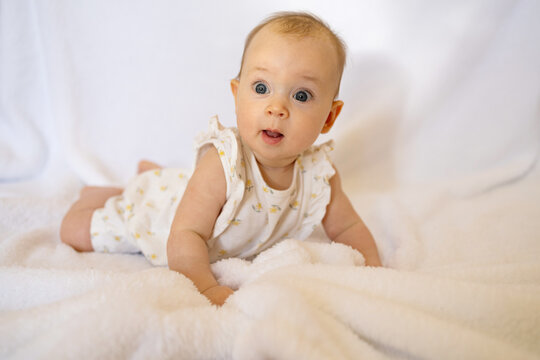 Baby girl in white sunny bedroom. Newborn child relaxing in bed. Nursery for children. Textile and bedding for kids. Family morning at home. New born kid during tummy time.