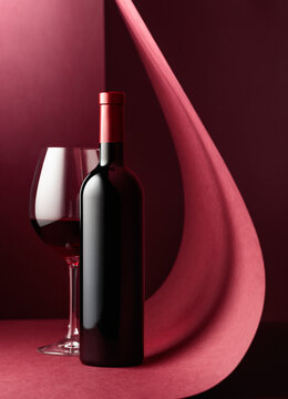 Bottle and glass of red wine on a red background.