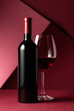 Bottle and glass of red wine on a red background.