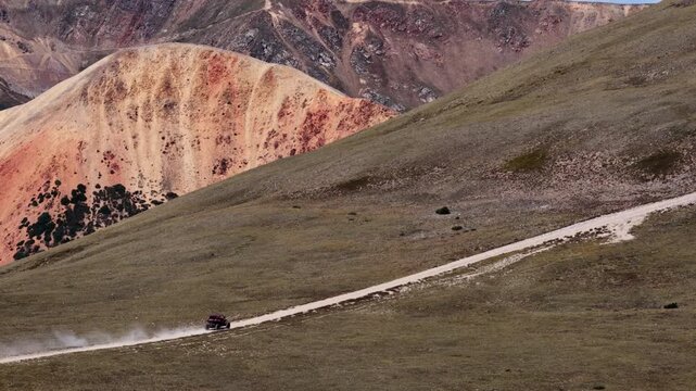 Aerial of UTV on dirt road through Pike National Forest on Red Cone Pass at timberline with prominent red earth mountains