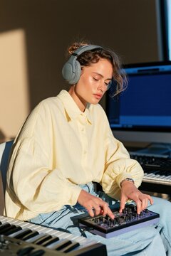 Young woman music producer wearing headphones working with a midi controller in a home studio for banner and background design