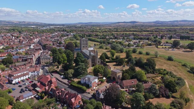 Aerial video of Tewkesbury in Gloucestershire, England, showcasing the historic townscape, residential areas, waterways, green spaces, and surrounding countryside from an elevated perspective