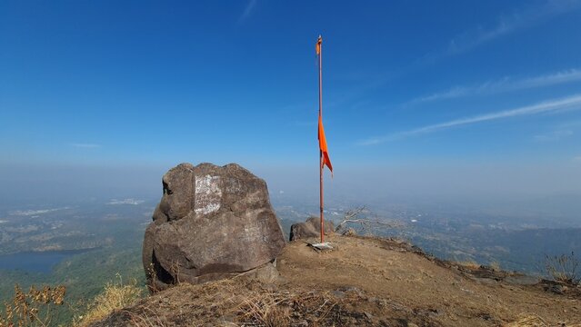 Saffron flag and rock formation overlooking Western Ghats landscape from mountain summit