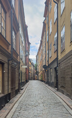Fototapeta premium Narrow cobblestone street lined with colorful historic buildings in Gamla Stan, the old town district of Stockholm, Sweden.