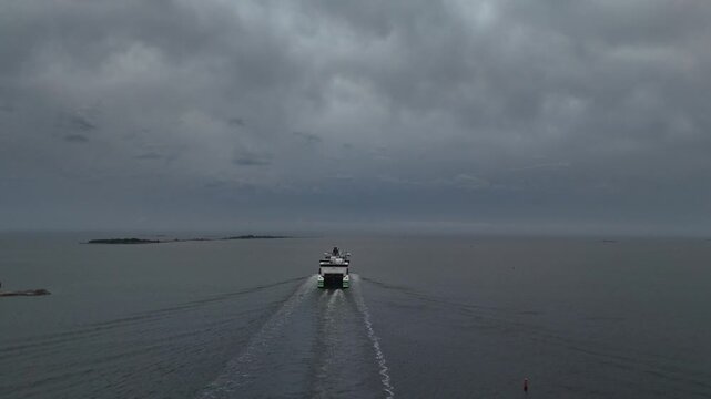 Drone footage of a passenger ferry moving farther into open water beneath heavy gray clouds with a dramatic horizon and darkening sea