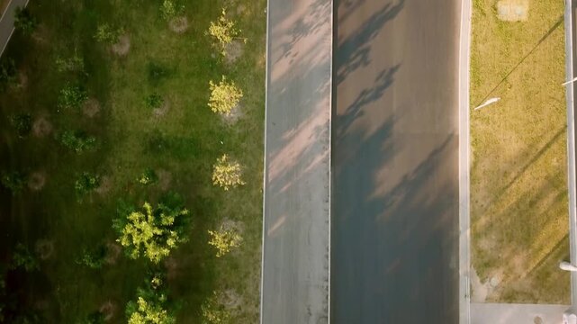Aerial top down view of runner on asphalt path next to green park with trees and children playground at sunset