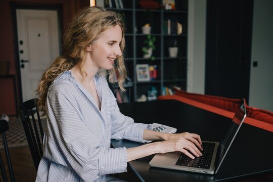 Woman typing on a laptop while working remotely from a modern home interior