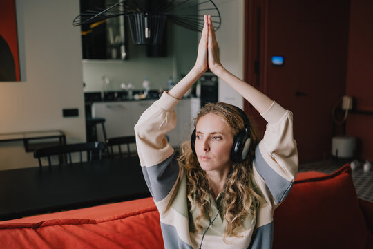 Woman stretching with headphones and raising hands above her head at home, combining mindful movement, relaxation and personal wellness in daily routine