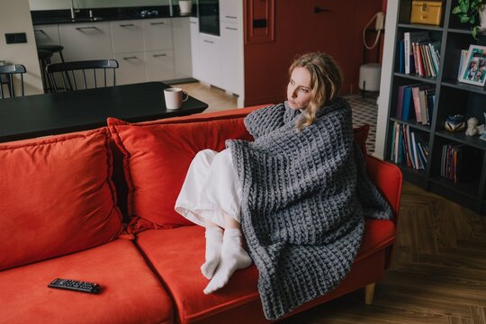 Woman wrapped in a thick blanket resting on a sofa and keeping warm at home