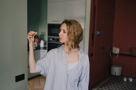 Woman holding and looking at keys while standing inside a modern home