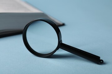Fototapeta premium Keywords. Magnifying glass and book on light blue background, selective focus. Space for text