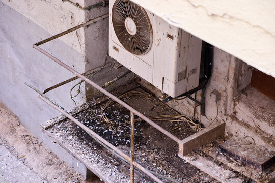 Dirty outdoor air conditioner unit covered in bird droppings and pigeon poop on old building facade wall with rusty metal railings, messy unsanitary urban scene, close up in Germany.