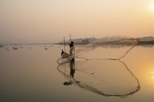 Fisherman with boat on Taung Tha Man Lake casts a fishing net for sunrise, reflection in the water, Thaung Tha Man Lake, Mandalay, Myanmar