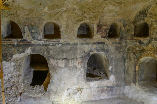 Sunlit wall of an ancient Roman tomb chamber lined with arched burial niches and painted garlands, Greece