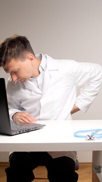 medical professional in a lab coat experiencing lower back pain while working long hours at a desk with a laptop, highlighting occupational health issues and discomfort