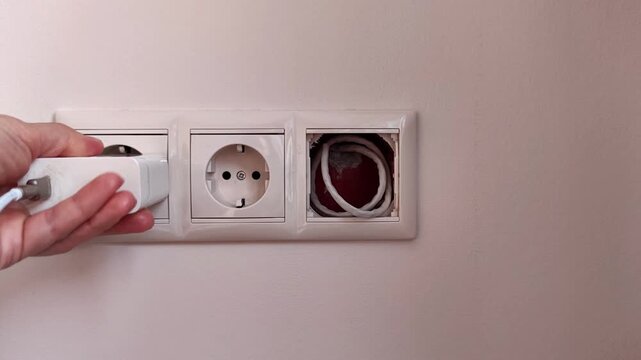 A hand inserts a white electrical plug into a wall outlet, demonstrating household power connection, home maintenance and electrical use.