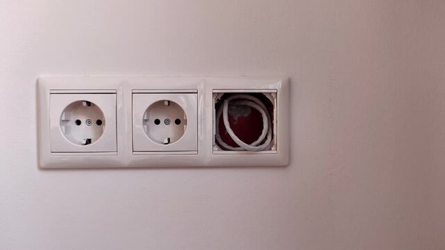 A hand pulls a white electrical plug out of the wall outlet, household electricity and safe power connection in a modern home interior.