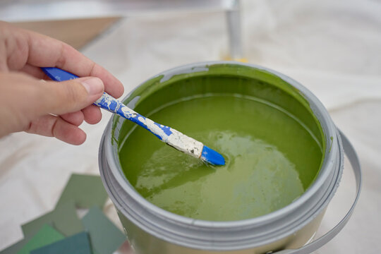 Hand mixes green paint with small brush in open paint can