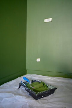 Green painted walls with paint roller and tray on protective floor covering