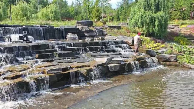 Worker using pond vacuum cleaner to clean artificial waterfall cascades in a park