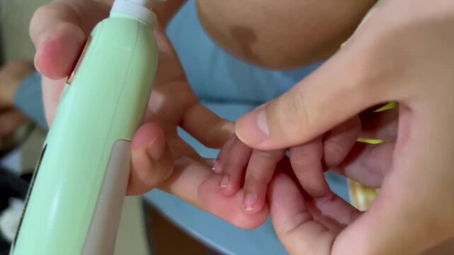 Parent trimming newborn baby nails using electronic nail file