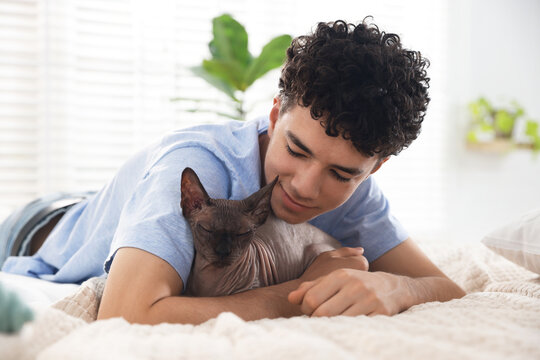 Teenage boy with Sphynx cat on bed at home. Adorable pet