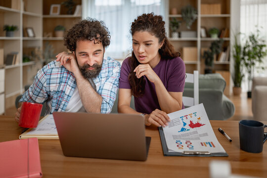 Young couple planning finances at home using laptop and printed reports during remote work session