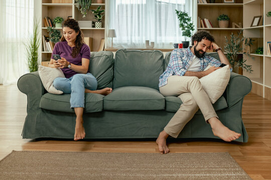Couple sitting apart on sofa using phones in bright living room