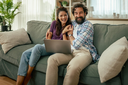 Smiling couple on couch using laptop together at home sharing a happy moment
