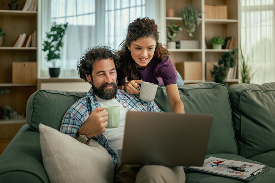 Couple on couch sharing coffee and working on a laptop in cozy living room