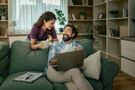 Couple working from home sharing coffee and laptop on a cozy living room sofa