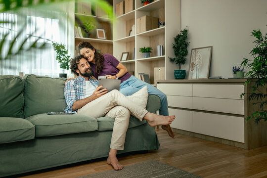 Couple relaxing on sofa at home sharing tablet and enjoying cozy moment in living room