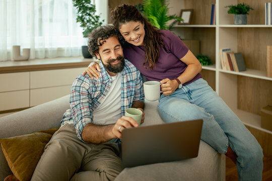 Young couple relaxing on couch with laptop and coffee in cozy living room