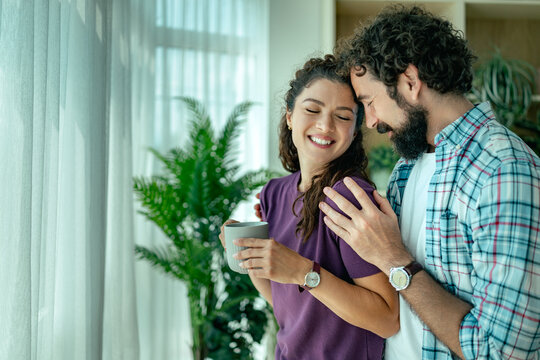 Young couple sharing a tender moment at home with coffee and affectionate embrace