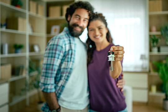 Young couple celebrating new home holding house key and smiling in living room